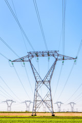 Front view of an electricity pylon in the french countryside with dozens of other pylons in the distance under a clear blue sky.