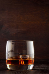 A glass of whiskey with ice on a wooden table
