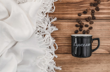 Side of black cup and beans with title espresso on the brown wooden table with white cloth