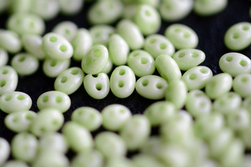 Twin beads light green color scattered on a dark surface close up