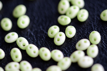 Twin beads light green color scattered on a dark surface close up