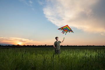 A child plays with a kite at sunset in the field.