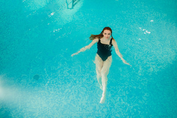 top view of a sexy beautiful reddish woman in black bath costume swimming backstroke in the swimming pool of a spa centre