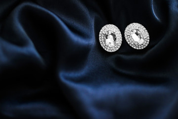 Luxury diamond earrings on dark blue silk background, holiday glamour jewelery present © Anneleven