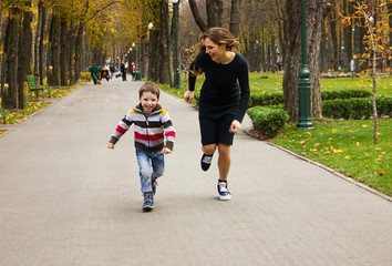 young stylish casual mother with her lovely child son are running in the autumn park and laughing happy. lifestyle sport concept, free space