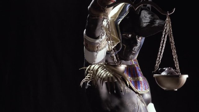 Anubis with jackal head is holding scales with golden fern leaf and a heart