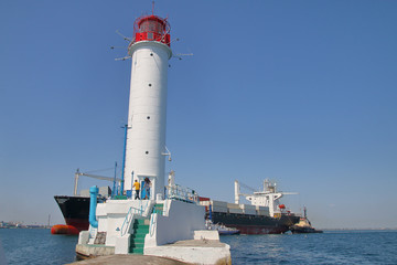 Modern container ship sailing near the old Odessa lighthouse.