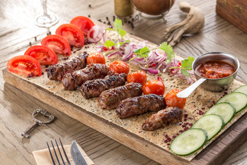 Barbecued kofta kebeb with onion and fresh tomato on lavash bread on wooden table