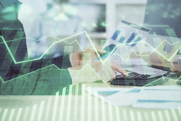 Double exposure of graph with man typing on computer in office on background. Concept of hard work. Closeup.