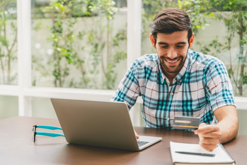 Handsome man holding credit card and using laptop for online shopping - indoors ,e-commerce concept