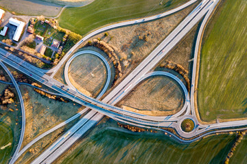 Aerial top view of modern highway road intersection, house roofs on spring green field background. Drone photography.