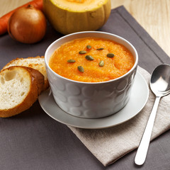Pumpkin soup with pumpkin seeds in a white plate. Two croutons near the soup.