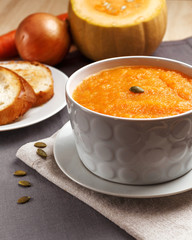 Pumpkin soup with pumpkin seeds in a white plate. Two croutons near the soup.