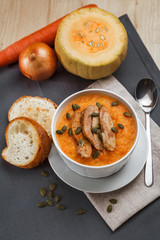 Pumpkin soup with smoked turkey and pumpkin seeds in a white plate. Two croutons near the soup.