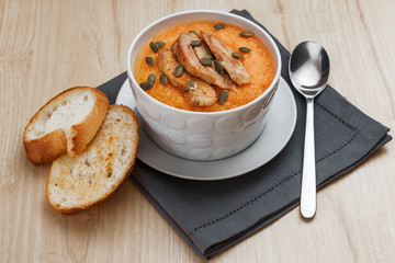 Pumpkin soup with smoked turkey and pumpkin seeds in a white plate. Two croutons near the soup.