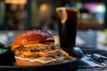 Beef hamburger served with fried potato, vegetables, coke and sauces  with blurred restaurant background . Melted cheddar