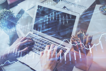 Double exposure of man's hands writing notes with laptop of stock market with forex graph background. Top View. Concept of research and trading.