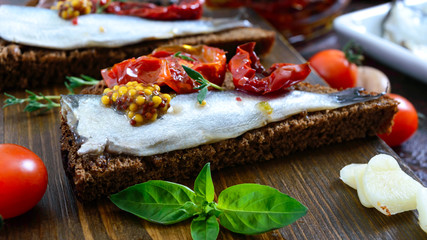 Tasty smorrebrod on a wooden board. Sandwiches with black rye bread, sun-dried tomatoes, salted anchovies, mustard.