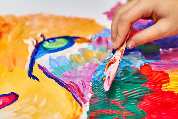 A girl paints a colorful lion on canvas using a brush and knife. Closeup, selective focus
