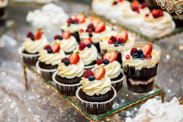 tea table, a lot of beautiful, bright and delicious cupcakes-cupcakes with cream, strawberries and blueberries