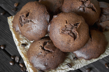 Homemade chocolate muffins on parchment with coffee beans. Dark wooden background, closeup, selective focus, top view
