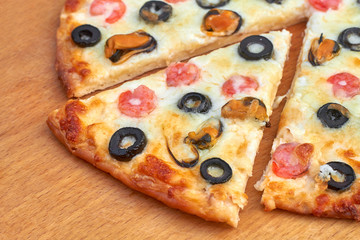 A part of homemade pizza with seafood on wooden board. Slice of homemade pizza with shrimp, mussels, black olives and mozzarella. Closeup, selective focus