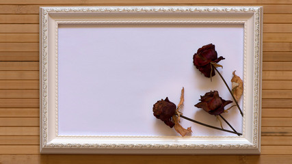 White frame with three dried red roses and empty white canvas on natural bamboo wall. Horizontal picture 16:9 with useful design for input your inside text, image etc.