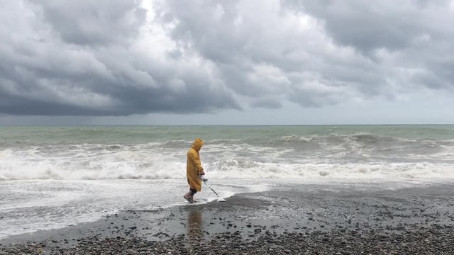 Man with a metal detector on the beach during a storm. A man is looking for jewelry on the beach. Storm clouds and large sea waves during a storm warning on the coast.