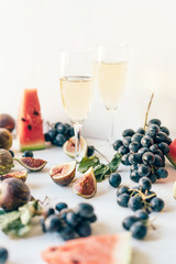 Tasty juicy appetizing food still life of fresh fruits and berries of the summer harvest on a white simple background with two glasses of white wine or champagne. Holiday concept. The couple in love.