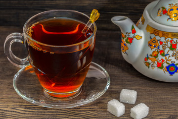 On wooden insulated floor, silver and porcelain teapot, cup of tea and crystal sugar on the floor.