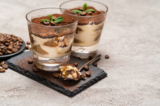 Portion of Classic tiramisu dessert in a glass cup on stone serving board on concrete background