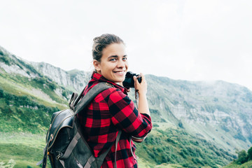 Portrait of a beautiful caucasian female photographer holding a camera in the mountains. Girl blogger makes a photo for his online blog. Journalistic content professional at work. Epic landscape.