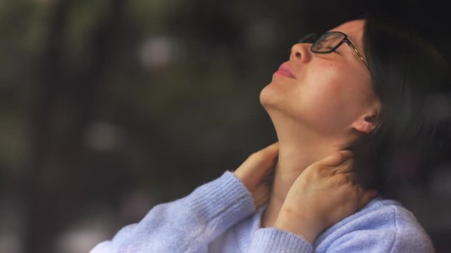 Close up of Asian woman sitting by the window feel neck pain and relax her neck then looking out of the window concept of working people health related issue 