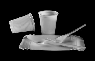 Disposable white paper plate, plastic cups and cutlery, fork and spoon for birthdays isolated on black background 