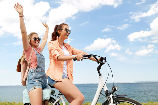 leisure and friendship concept - happy smiling teenage girls or friends riding bicycle together at seaside in summer