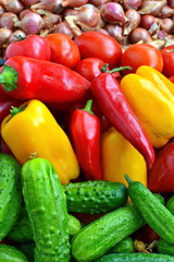 Green cucumbers, large red and yellow sweet peppers, red ripe tomatoes and bulbs onion in large quantities on the shelves store. Close up. Vegetable background