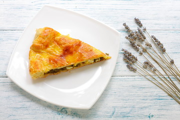 A piece of cake with liver and egg on a white plate. Puff pastry liver cake. Cold tasty snack. One serving of meat flour products. Golden pie stuffed with filling on wooden vintage table.