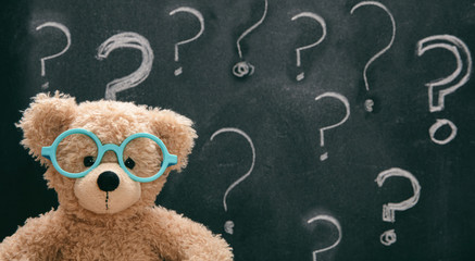 Cute teddy wearing glasses against blackboard with a question mark