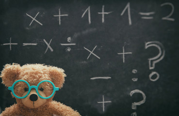 Cute teddy wearing glasses and black chalkboard with mathematics