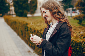 beautiful stylish young girl with long curly hair and a long coat and glasses standing in the autumn city and uses the phone