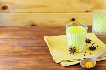 Golden milk from turmeric, vegetable milk, pepper, ginger, coconut oil, maple syrup in a glass on a wooden table. Traditional indian drink.