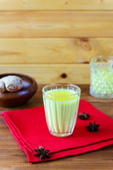 Golden milk from turmeric, vegetable milk, pepper, ginger, coconut oil, maple syrup in a glass on a wooden table. Traditional indian drink.