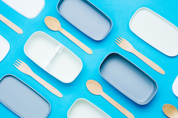 Llunch boxes with wooden forks and spoons on blue background