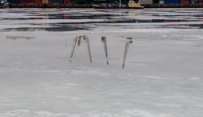 reflection of harbor cranes in melting ice