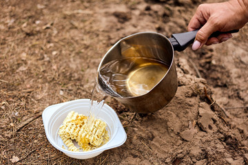 Woman's hand pouring boiling water on instant noodles in the forest.