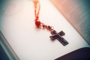A black Gothic cross with black beads on a chain lies on an open book for black magic and dark rituals.