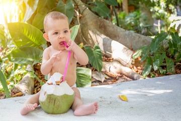 Happy infant baby at tropical vacation. Eats and drinks green young coconut.