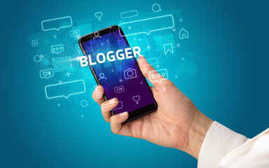 Female hand typing on smartphone with BLOGGER inscription, social media concept