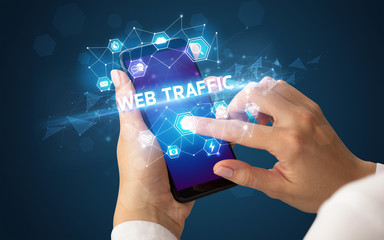 Female hand holding smartphone with WEB TRAFFIC inscription, modern technology concept