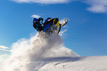 snowmobile jump. bright snowmobile in motion. the guy is flying on a snowmobile on a background of blue sky leaving a trail of splashes of white snow. bright snowmobile and suit without brands. super